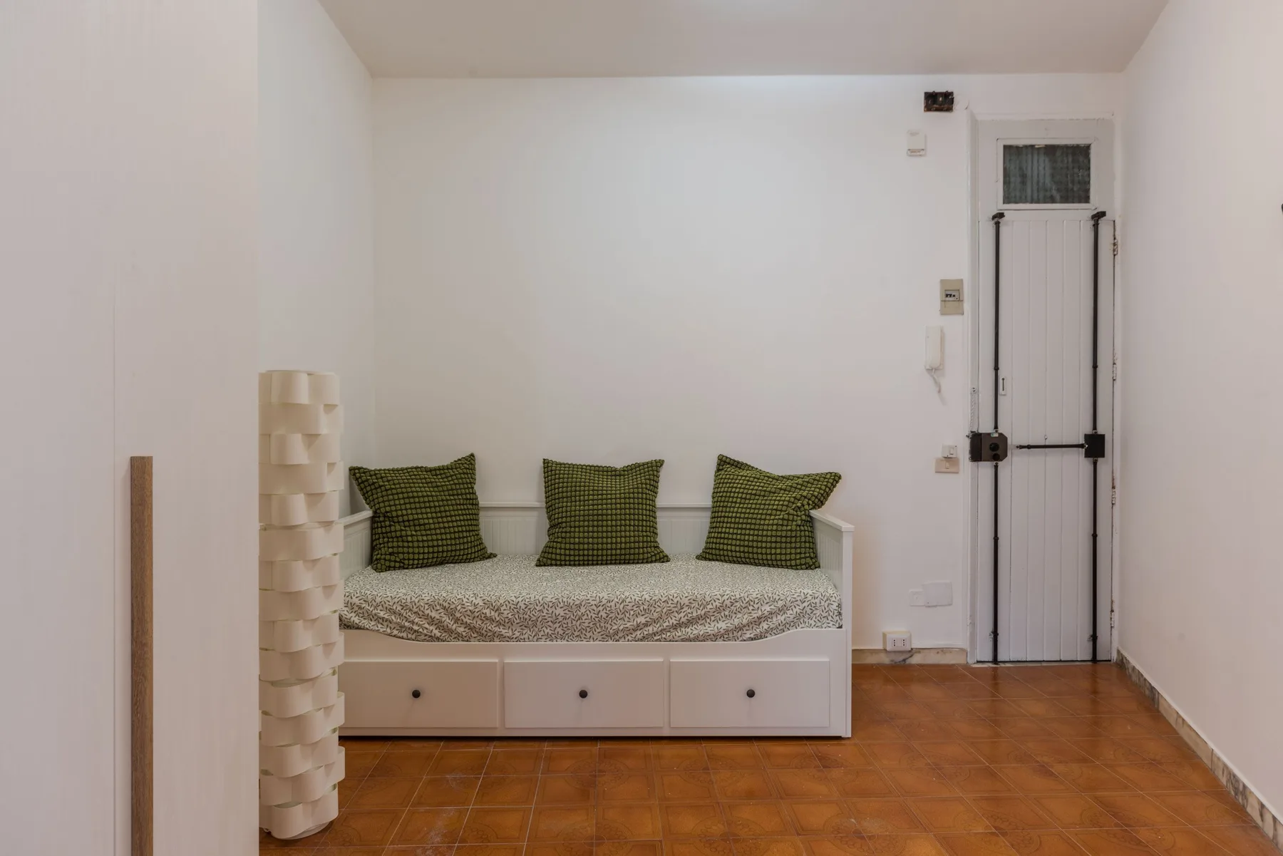 A compact bedroom with a daybed, patterned cushions, and tiled flooring.