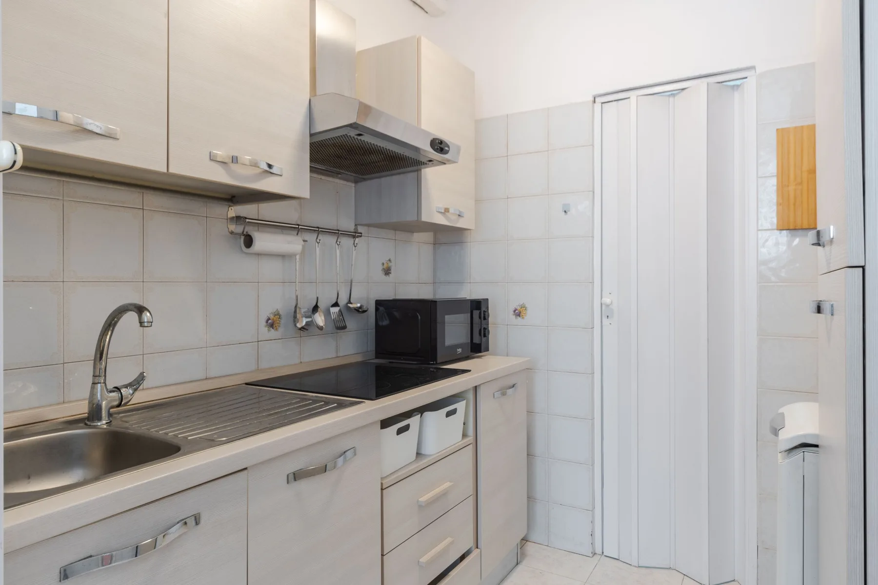 A compact kitchen with a sink, cooktop, and white cabinets.