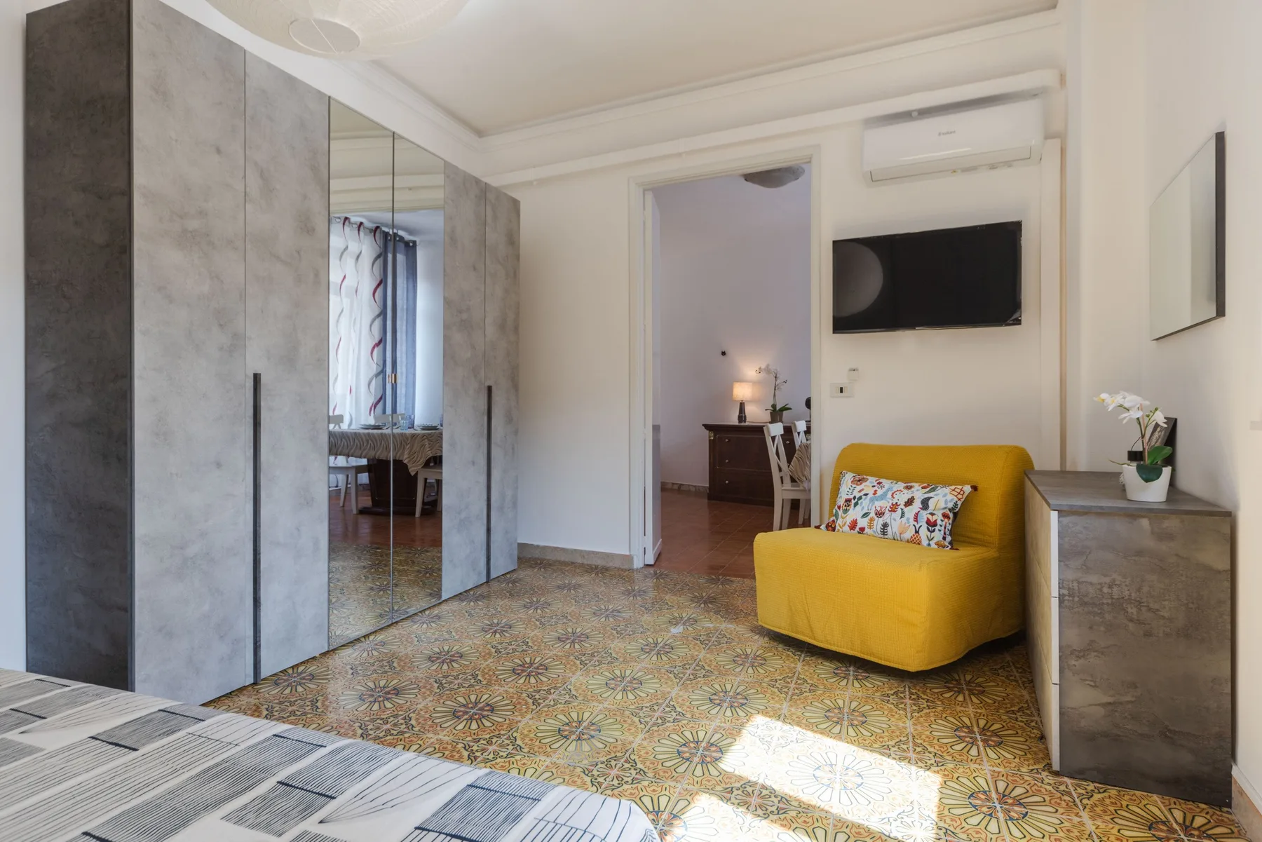 A bedroom with a yellow armchair, wardrobe, and television.