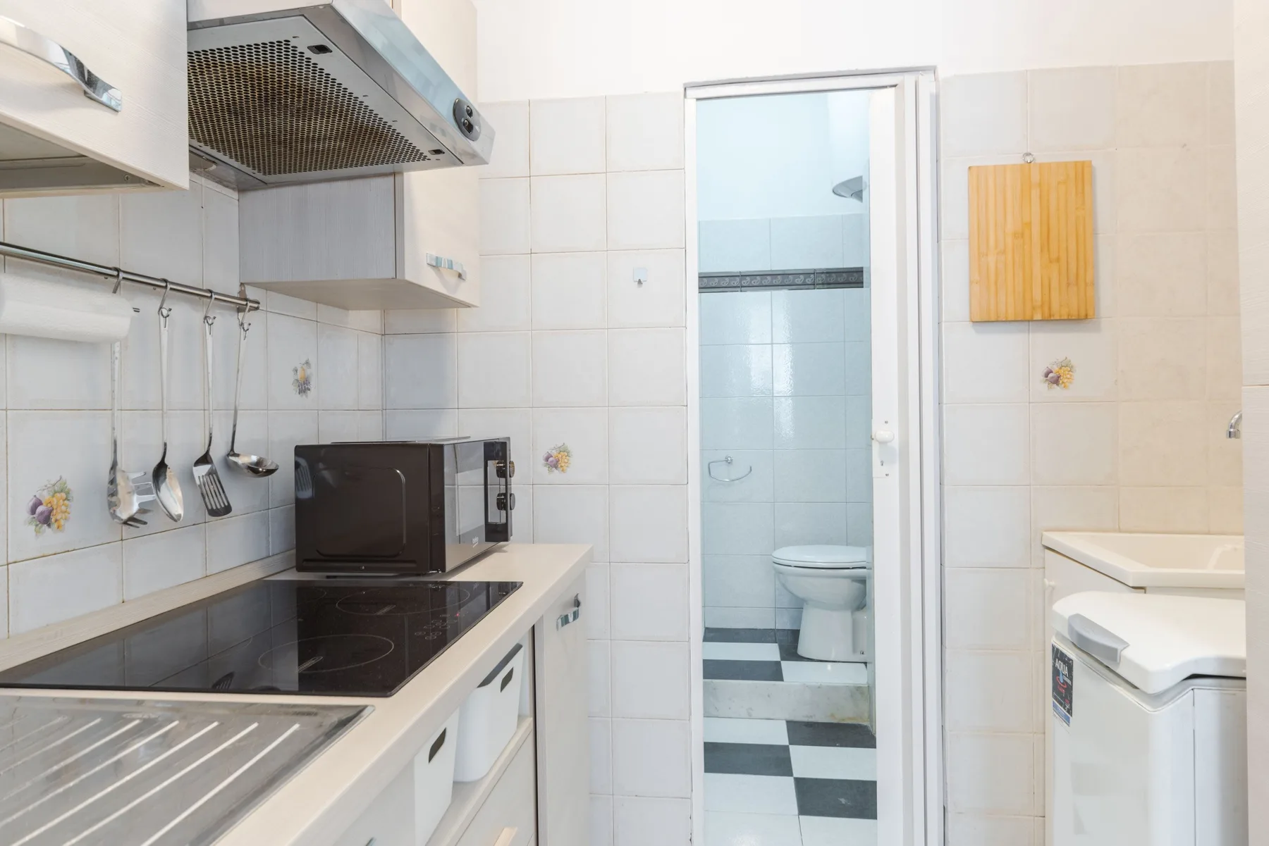 A tiled kitchen with a stovetop and counter beside an open bathroom doorway.