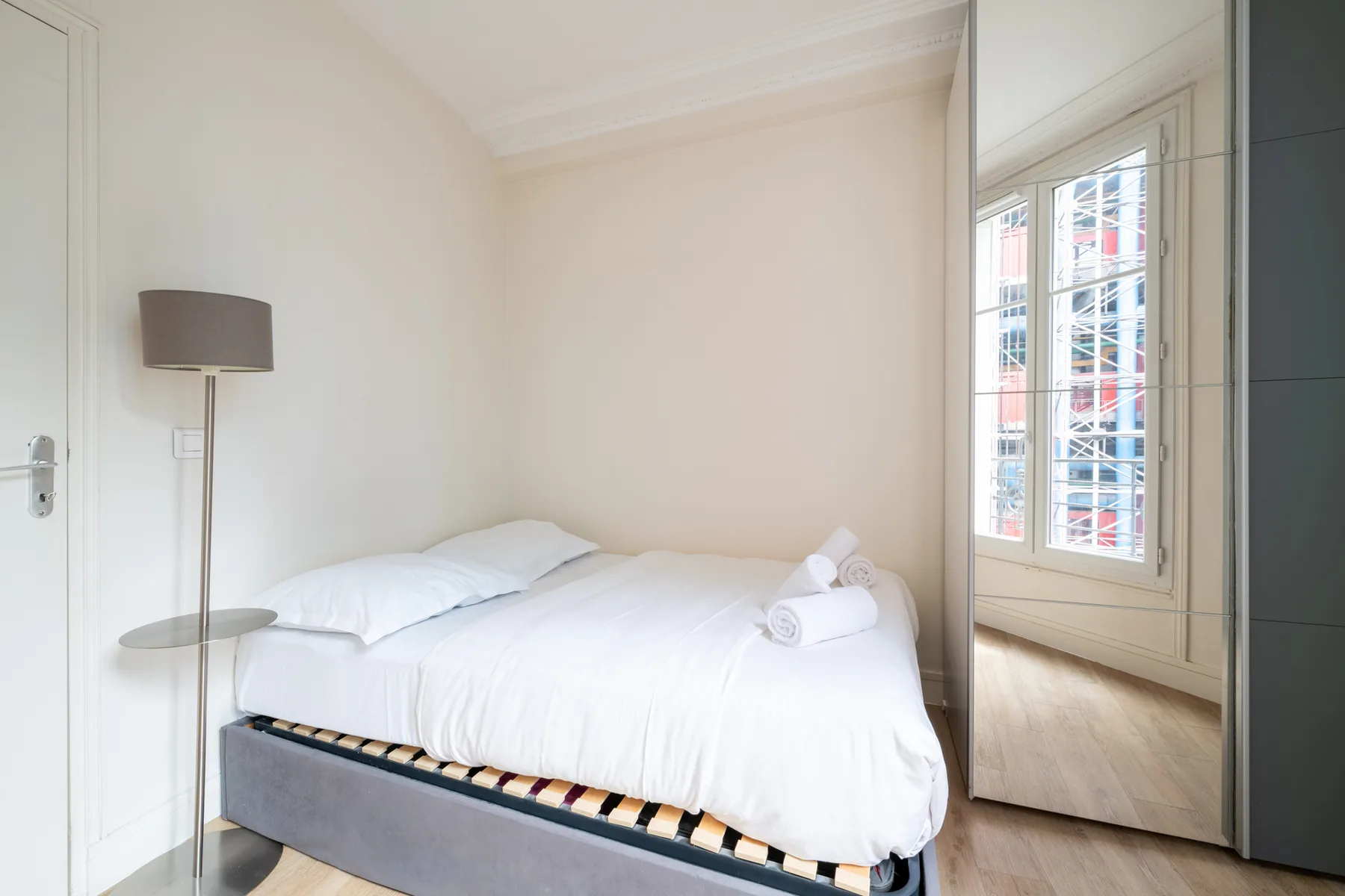 A bedroom with a neatly made bed and a mirrored wardrobe.