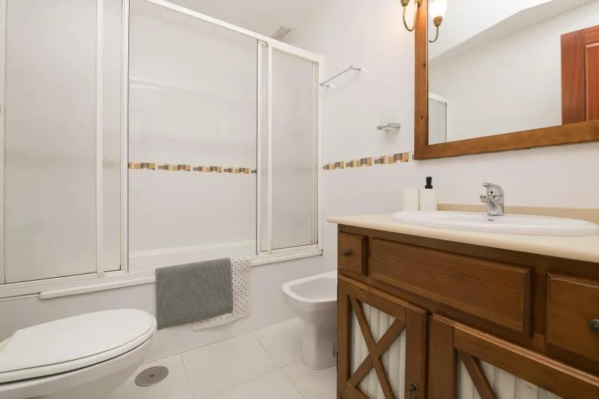A bathroom with a bathtub, toilet, and wooden vanity beside a sink.