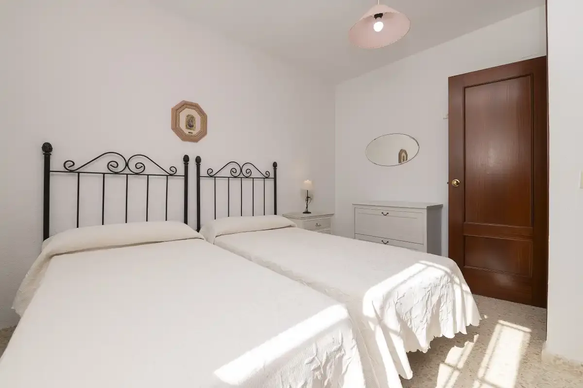 A bright bedroom with two beds and dark metal headboards.