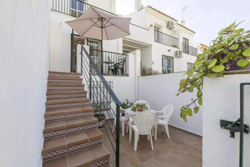 A tiled outdoor patio with white seating sits beside a staircase and umbrella.