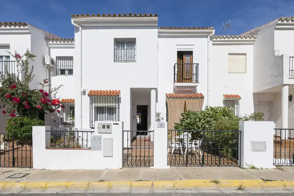 White two-story townhouses line a street behind small front gardens and metal gates.