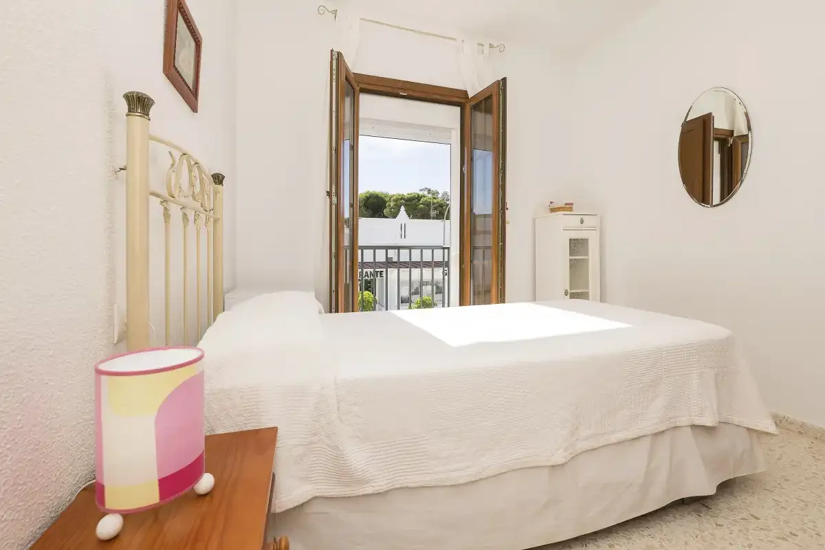 A bedroom with white bedding and open doors leading to a balcony.