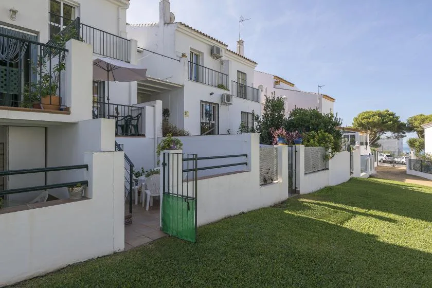 White residences with balconies line a grassy courtyard beside a green gate.