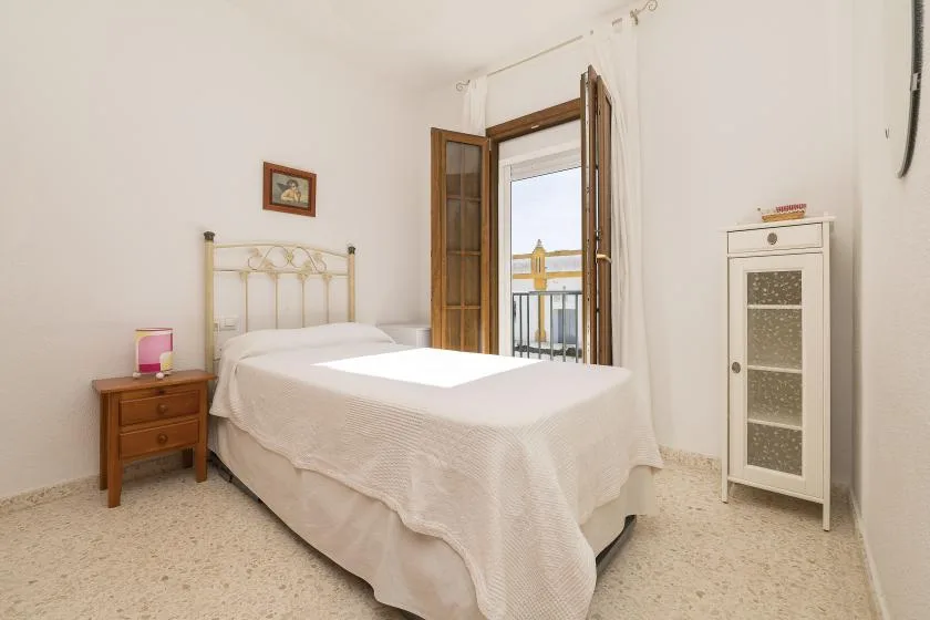 A bedroom with a bed, bedside table, and an open balcony door.