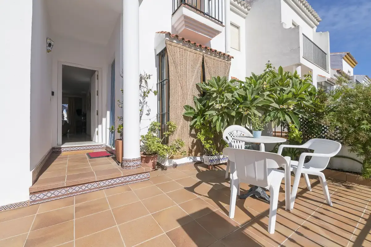 A tiled patio with white outdoor seating and potted plants beside a house.