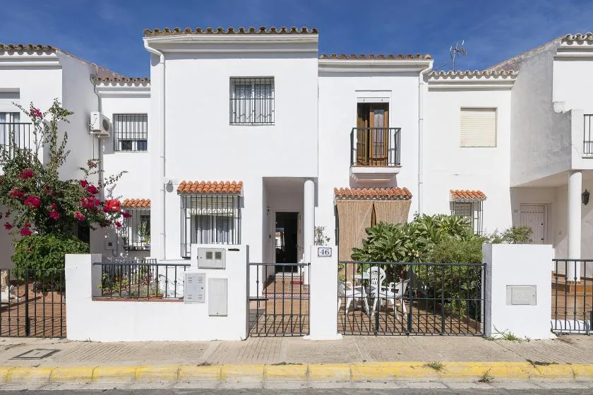 White townhouses with balconies and gated front patios line a sunny street.