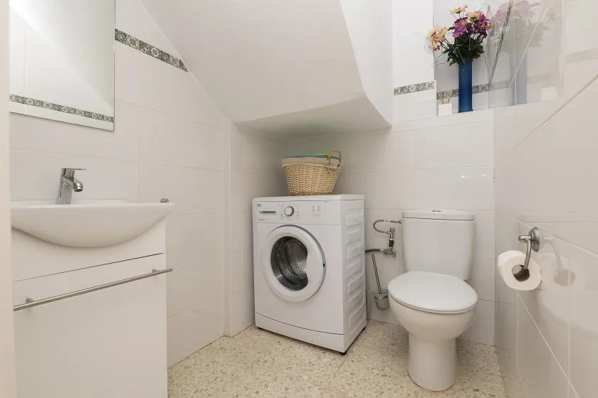 A bright bathroom with a sink, washing machine, and toilet.