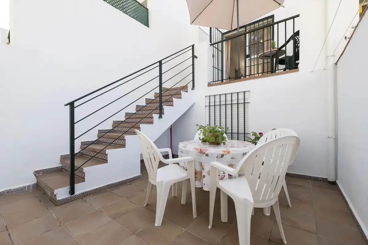A tiled patio has a table and plastic seating beneath a staircase.