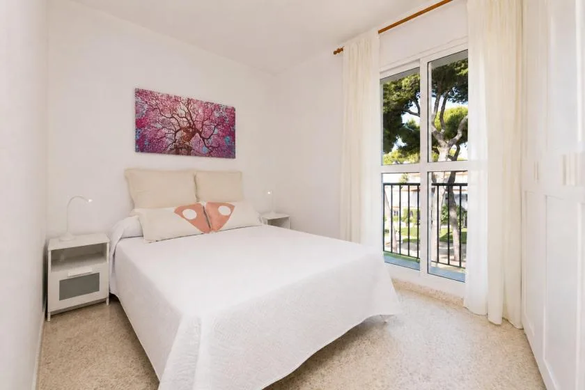 A bright bedroom with a white bed and a large window overlooking trees.