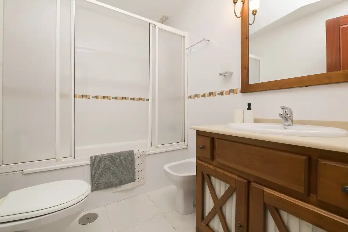 A bathroom with a bathtub, toilet, and wooden vanity.