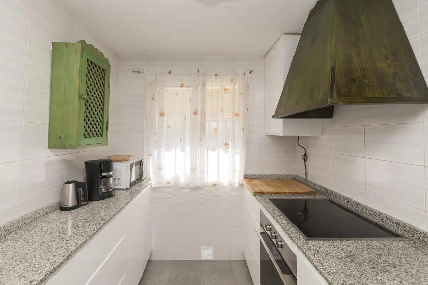 A bright kitchen with white cabinets, countertop appliances, and a window with sheer curtains.