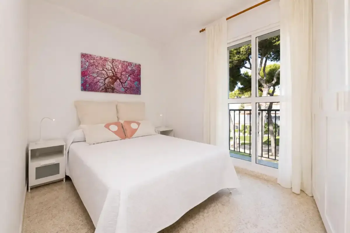 A bright bedroom with a neatly made bed and a window overlooking trees.