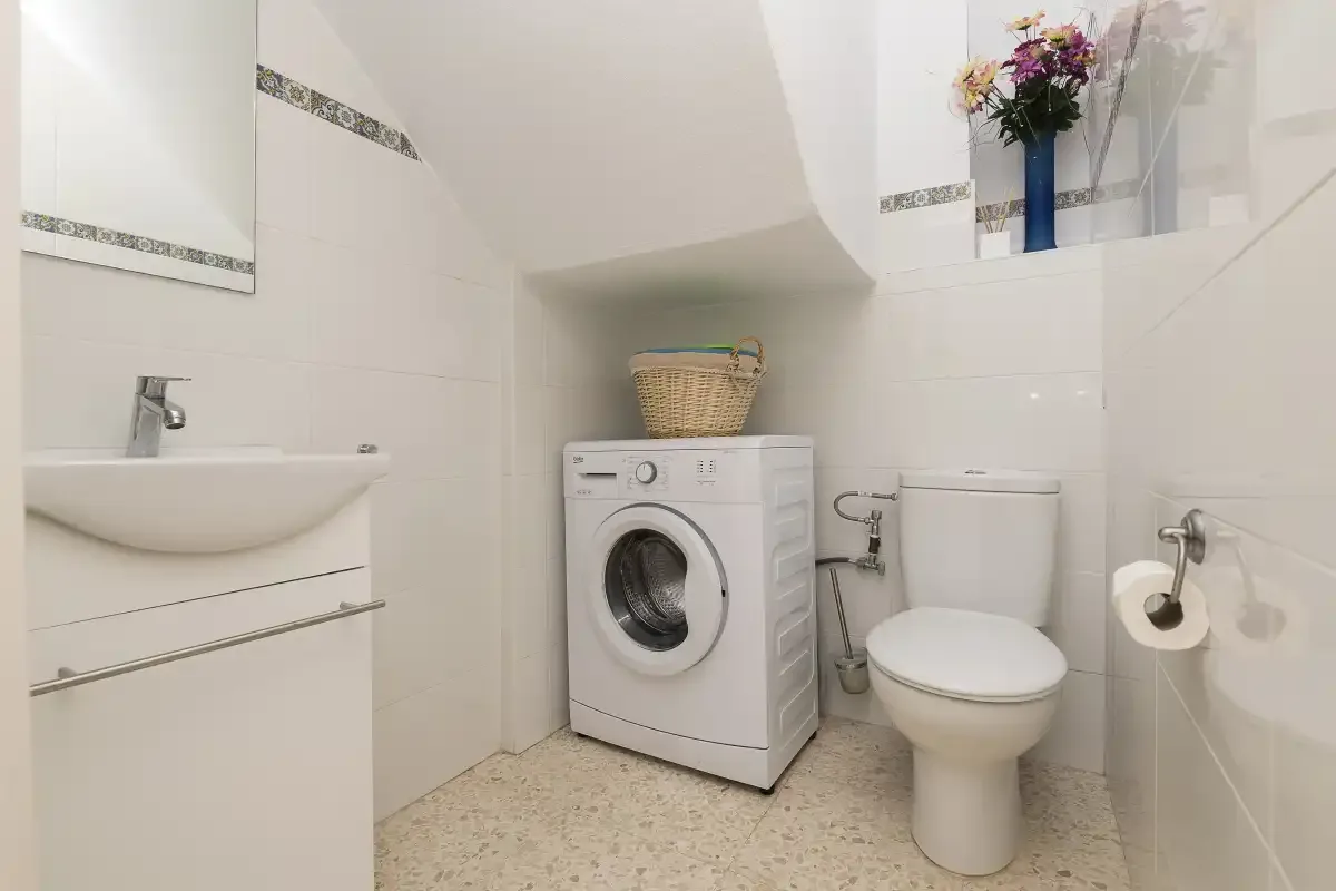 A bright bathroom with a washing machine, sink, and toilet.