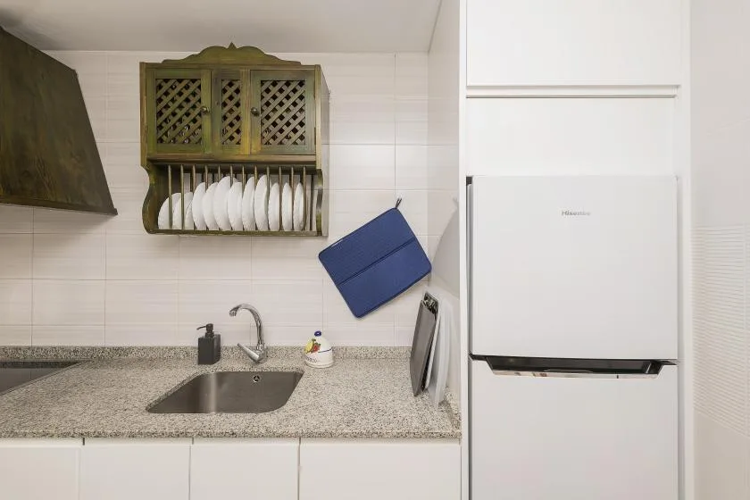 A compact kitchen with a sink, countertop, dish rack, and refrigerator.