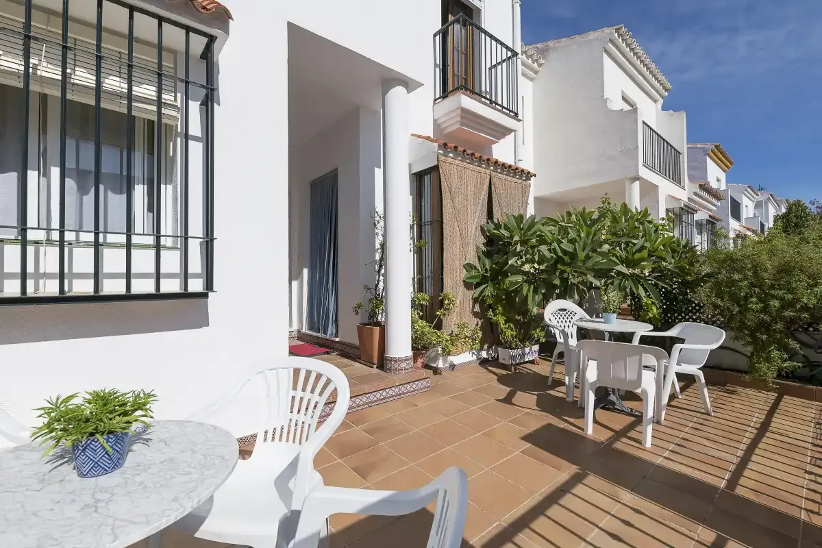 A sunny outdoor patio with white seating and a leafy hedge.