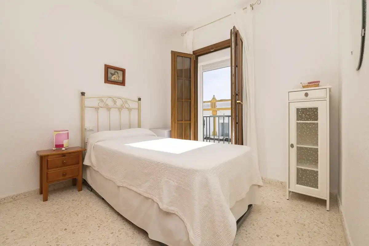 A bedroom with a neatly made bed beside an open balcony door.