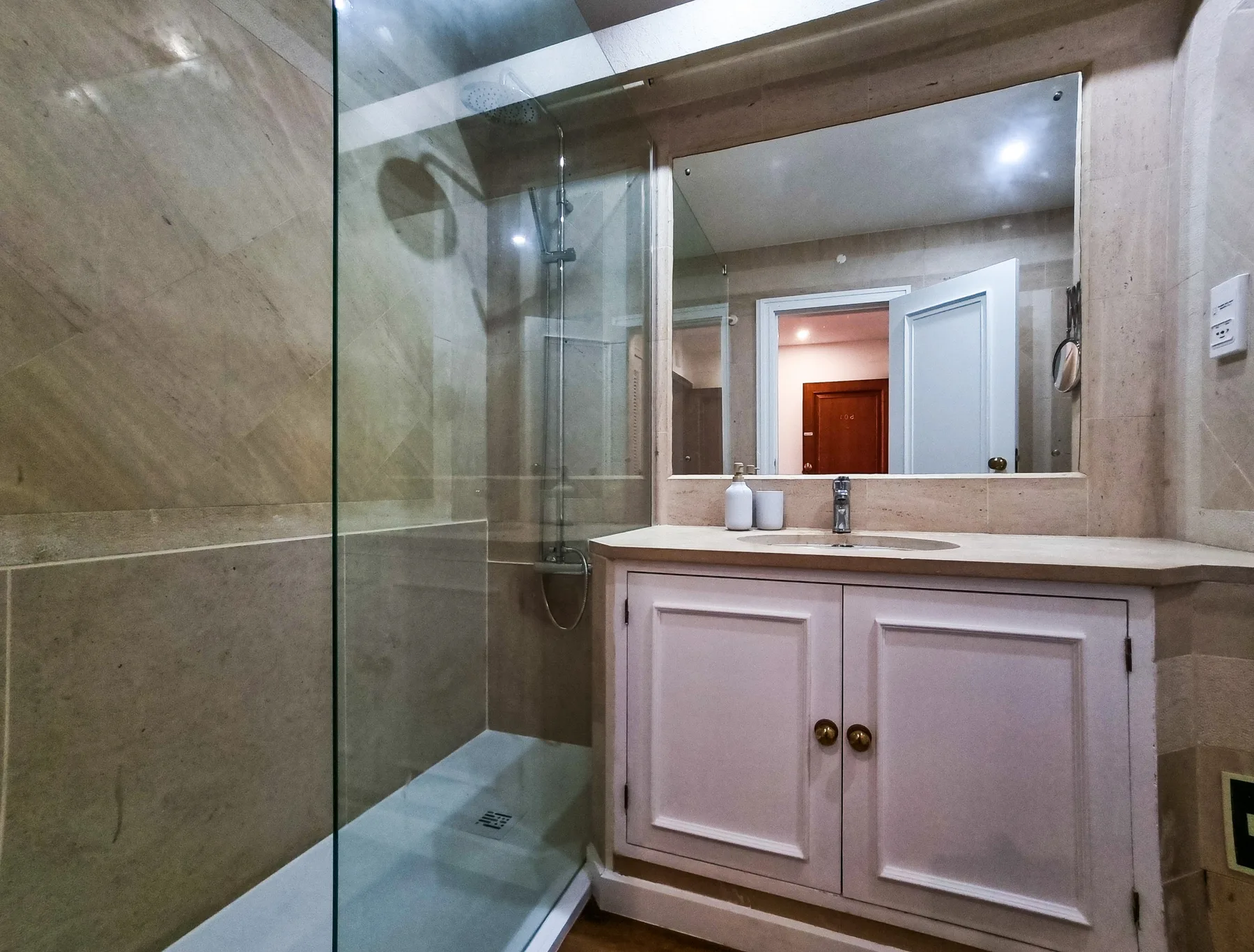 Un baño con una ducha de cristal y un lavabo bajo un espejo amplio.