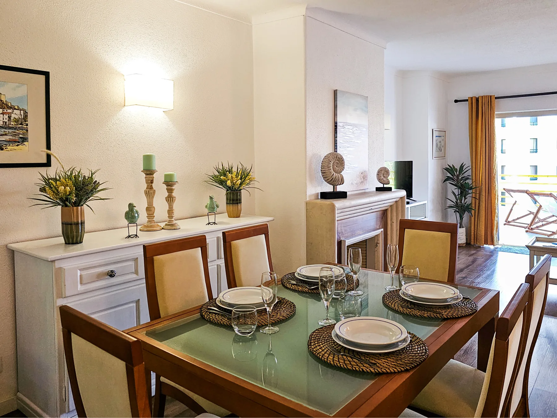 Comedor con la mesa puesta y un balcón luminoso al fondo.
