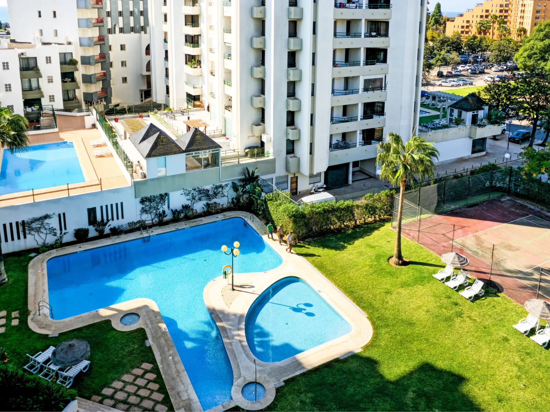 Se ven piscinas al aire libre y un césped junto a edificios de apartamentos.