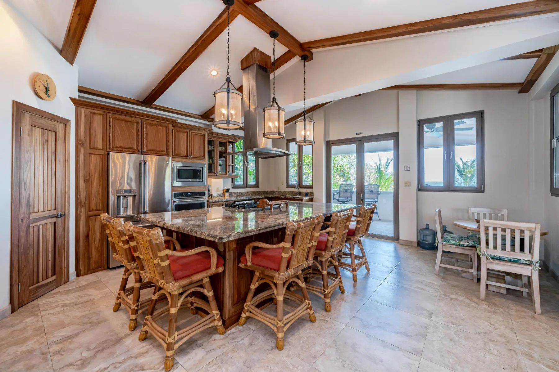 A spacious kitchen and dining area features a large island with seating beneath exposed wooden beams.