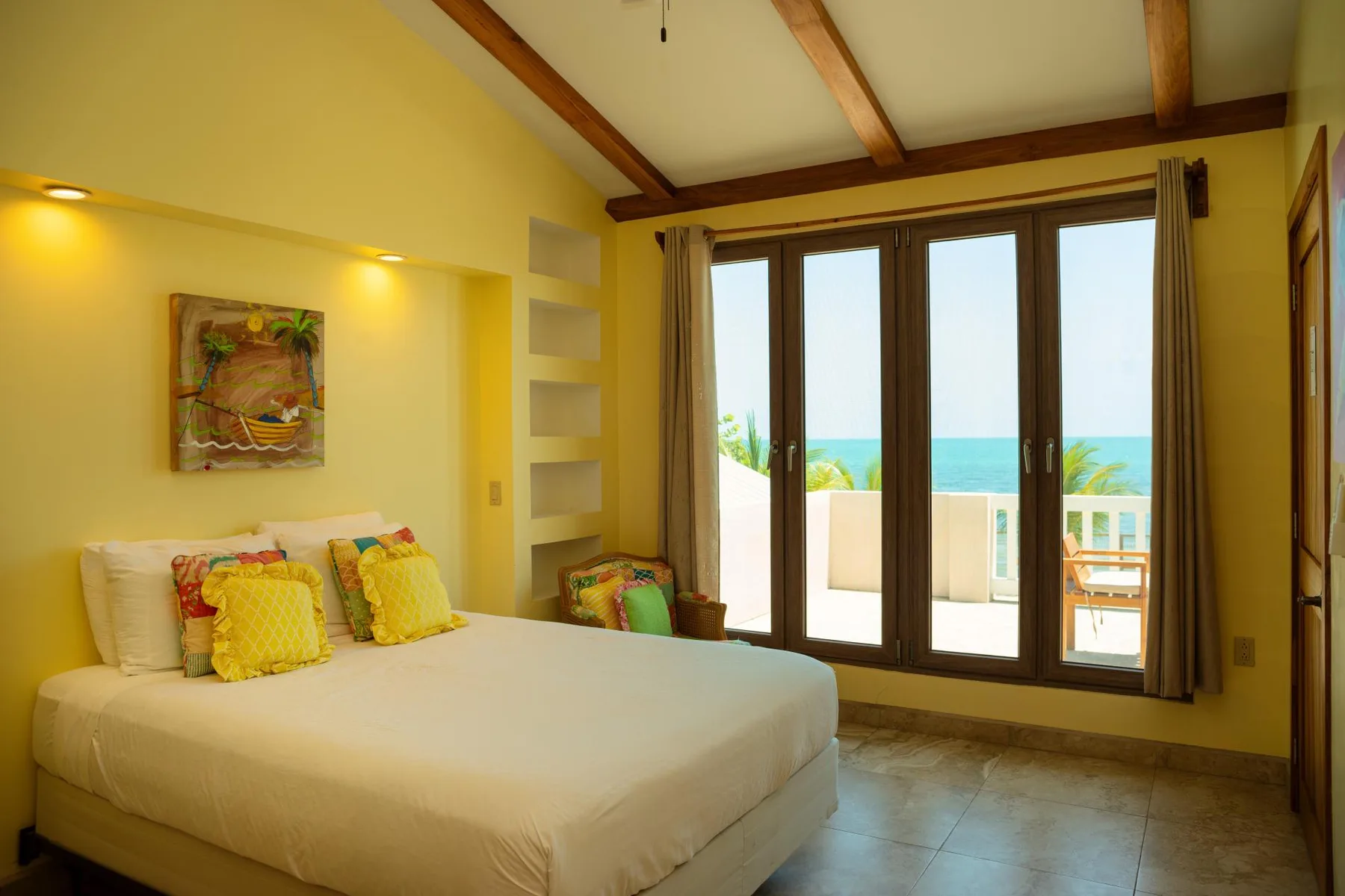 A bedroom with a bed beside tall windows overlooking the sea.