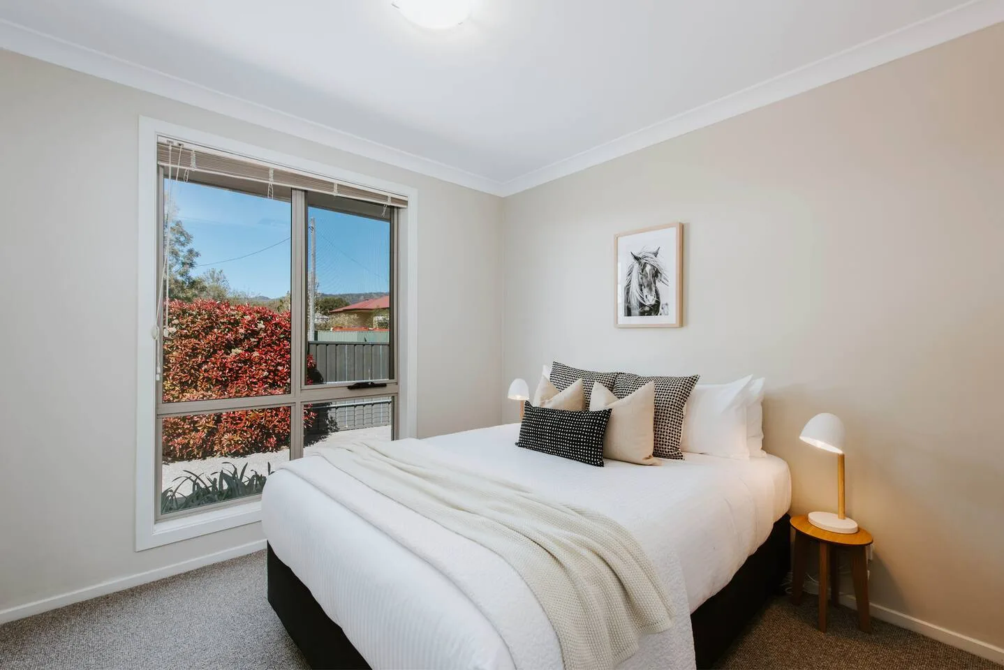 A bedroom with a bed beside a large window overlooking greenery.