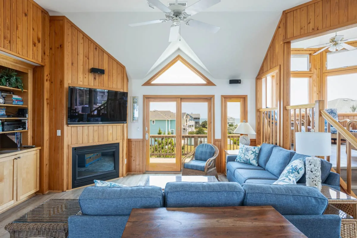 Una sala de estar revestida de madera, con asientos azules y puertas de vidrio que dan a un balcón.