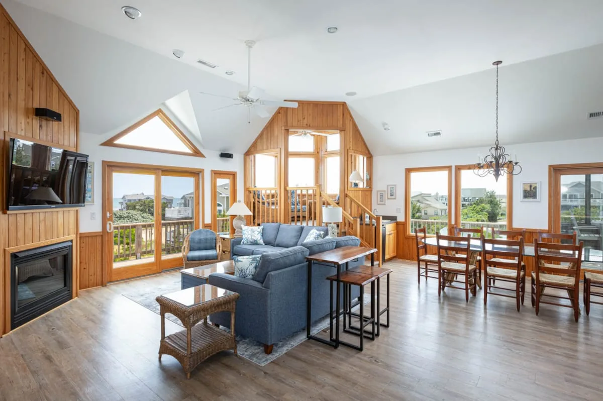Una sala y comedor abiertos cuentan con asientos, una mesa de madera y ventanas grandes.