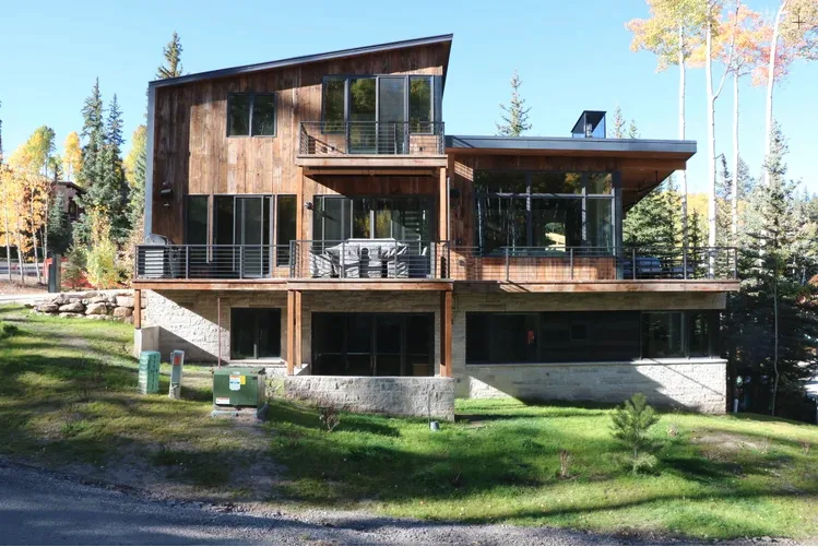 Una casa moderna con revestimiento de madera, grandes ventanas y una amplia terraza exterior.