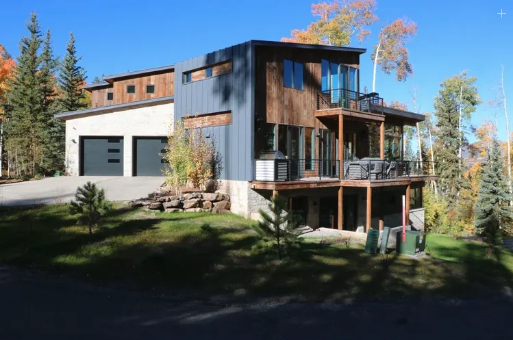 Una casa moderna con un garaje amplio y una terraza de madera elevada entre árboles.