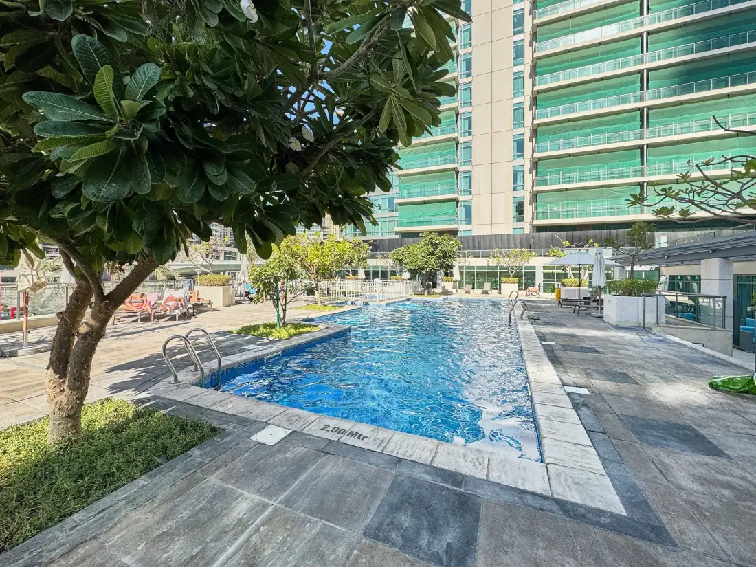 Una piscina al aire libre está junto a una terraza pavimentada y árboles.