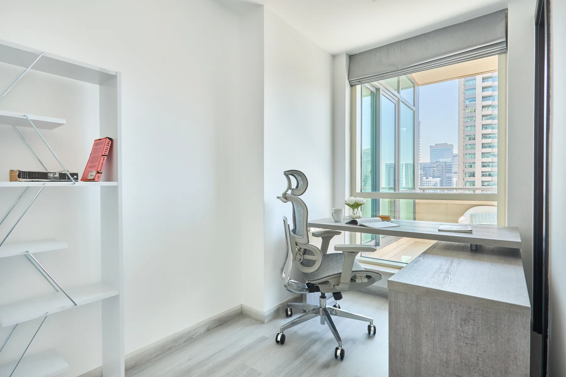 Un espacio de trabajo luminoso con escritorio, silla de oficina y grandes ventanas con vista a edificios.