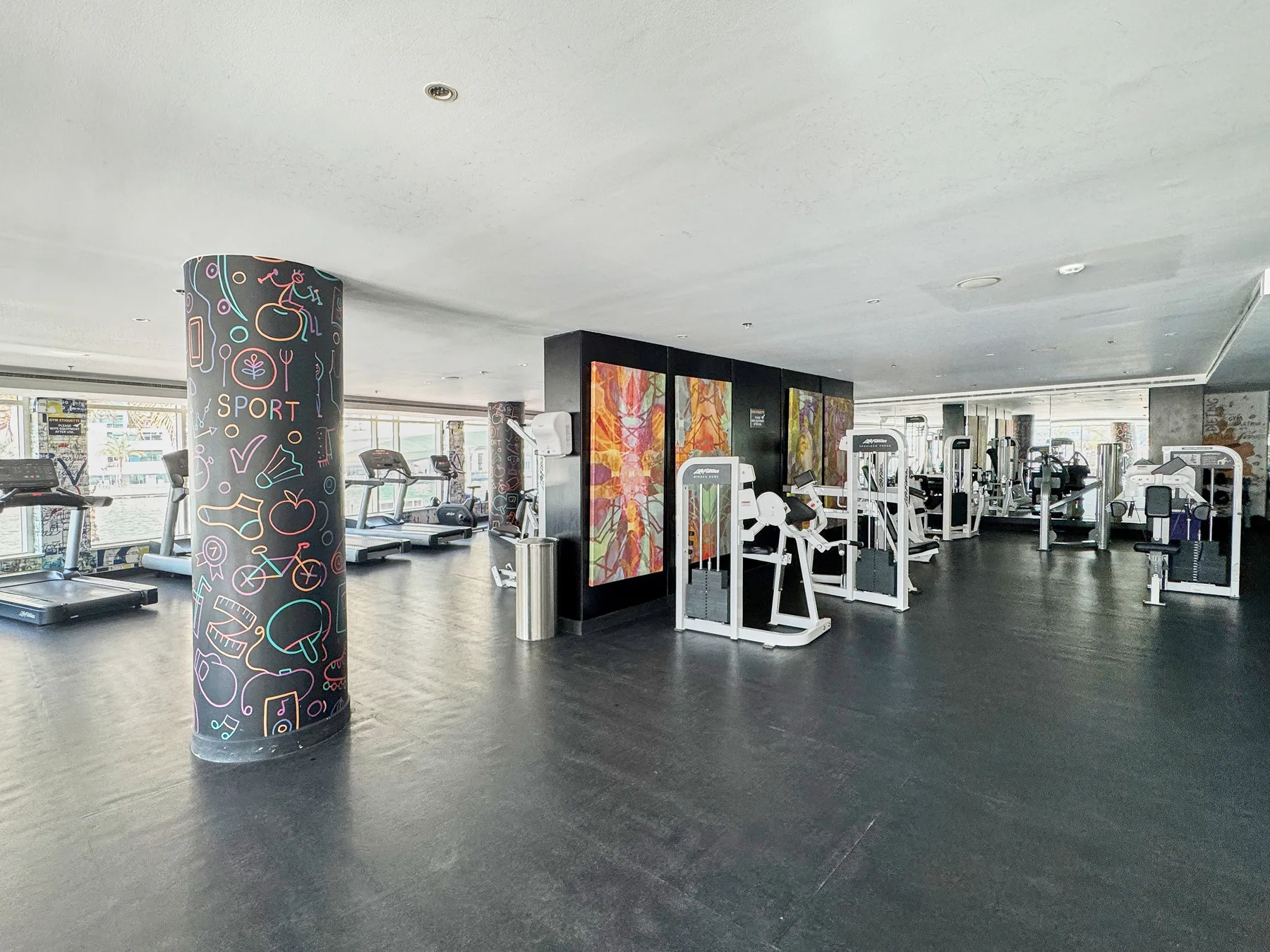 Un gimnasio con máquinas de ejercicio y una columna con ilustraciones coloridas.