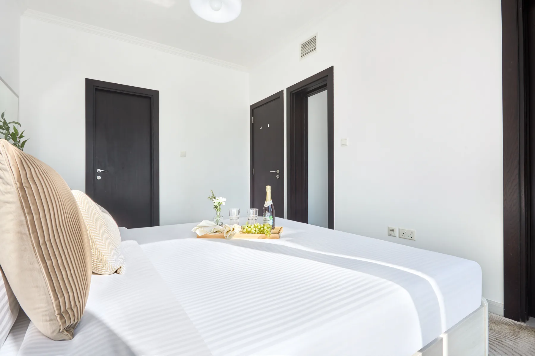 Un dormitorio luminoso con ropa de cama blanca y una pequeña bandeja sobre la cama.
