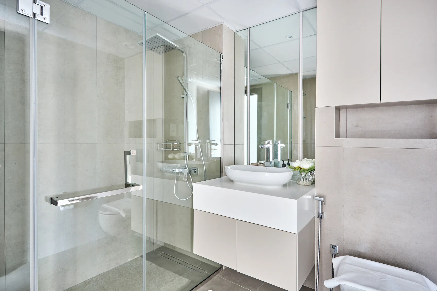 Un baño luminoso con una ducha de vidrio y un lavabo blanco.