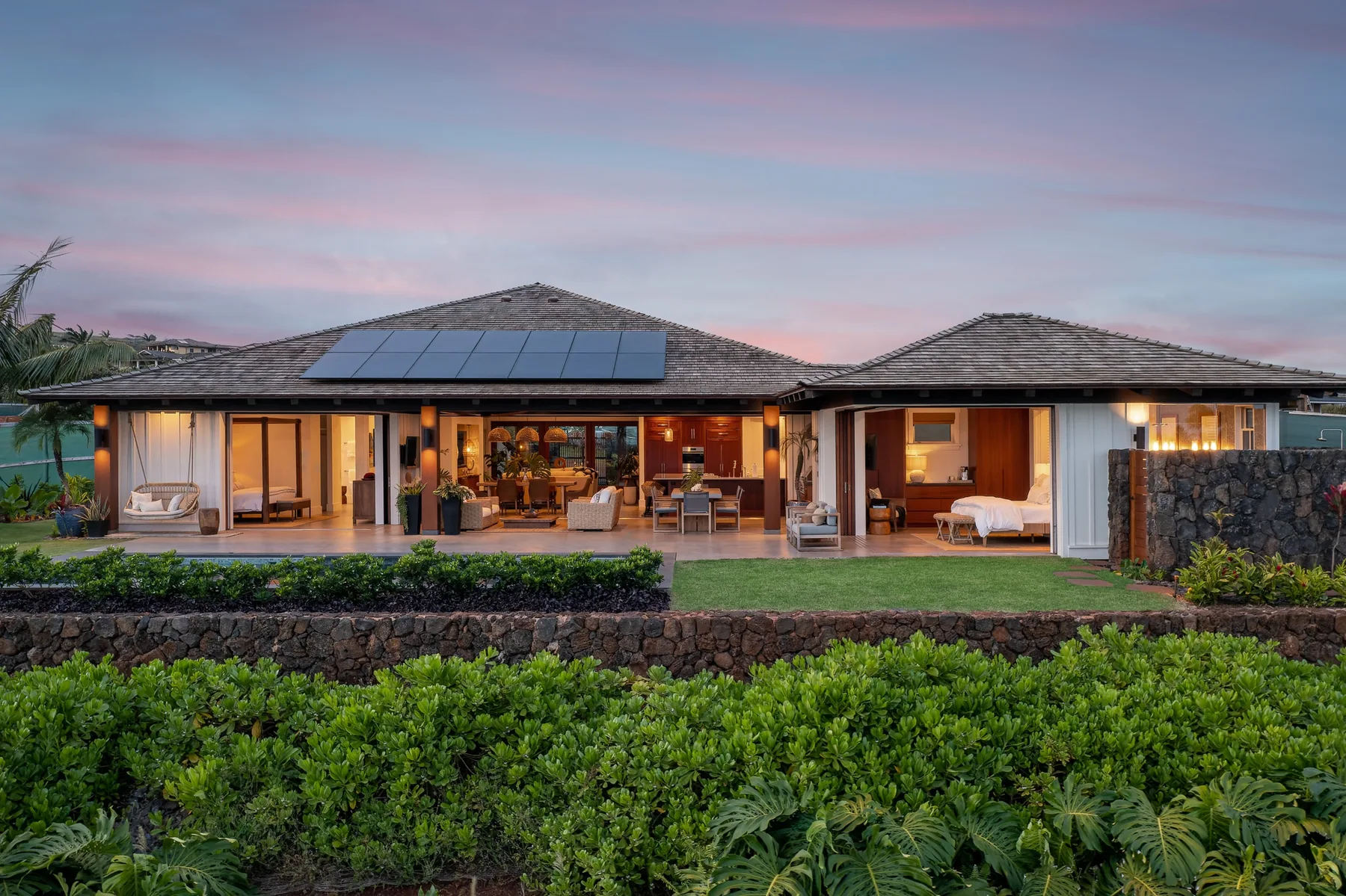 A single-story house opens onto a patio with seating and a garden at dusk.