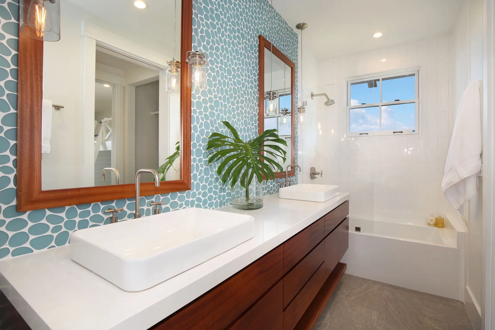 A bright bathroom with a double vanity, patterned tile backsplash, and bathtub.