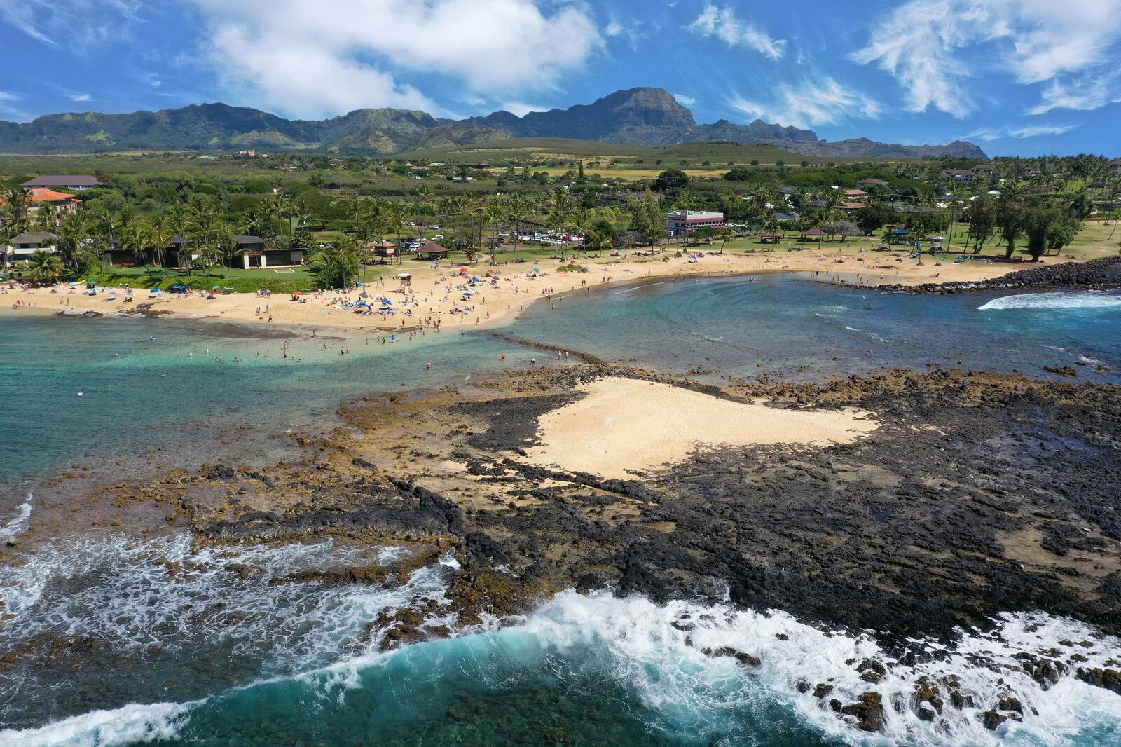 Aerial view of a sandy beach and turquoise water with mountains in the distance.