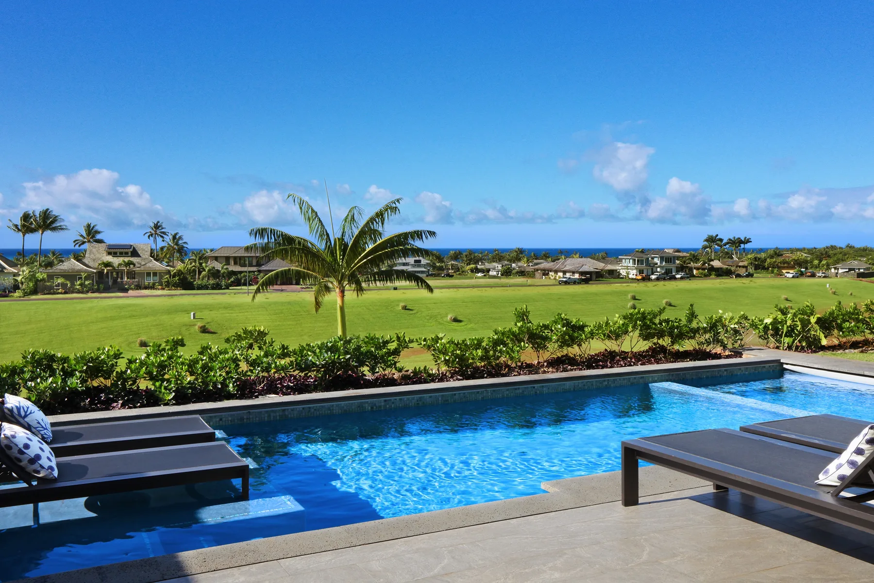 A swimming pool overlooks a green lawn and the ocean.
