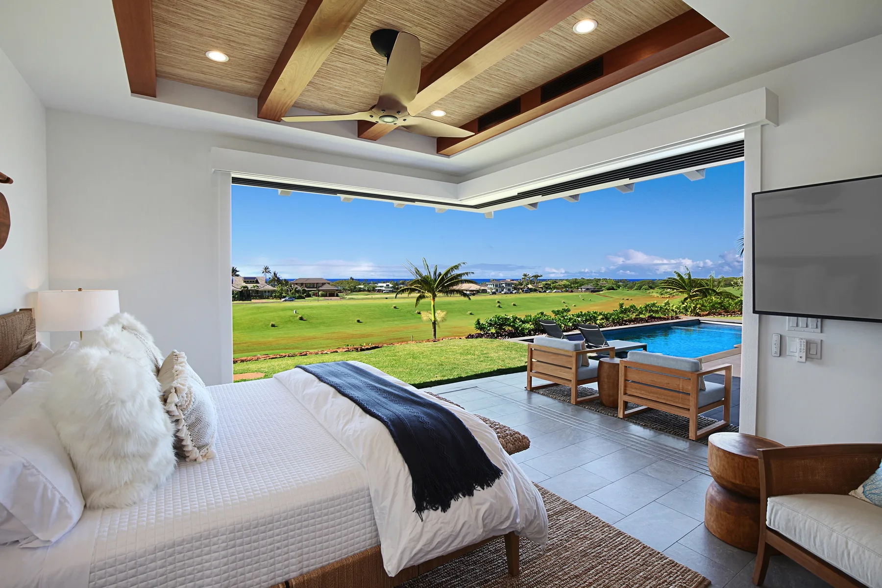 A bedroom opens onto a patio with seating and a pool overlooking a green landscape.