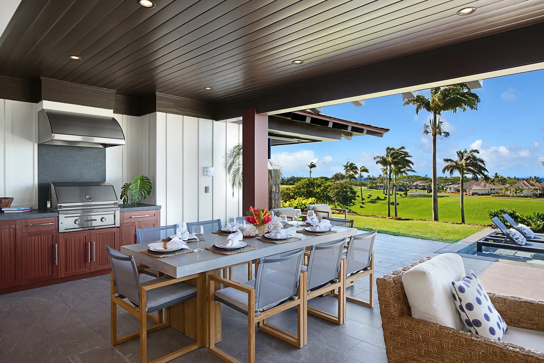Covered outdoor dining area with a table and seating overlooking a landscaped lawn.