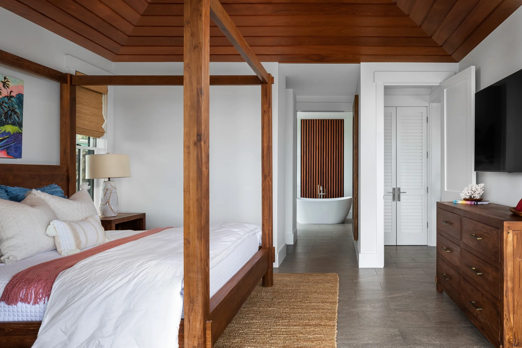 A bedroom with a wooden canopy bed and a freestanding bathtub in the adjoining bathroom.