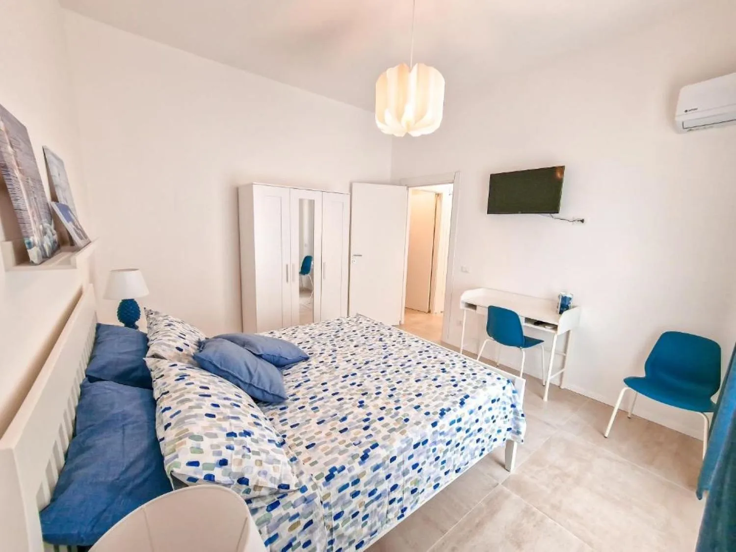 A bedroom with a patterned bed, a small desk, and a wall-mounted television.