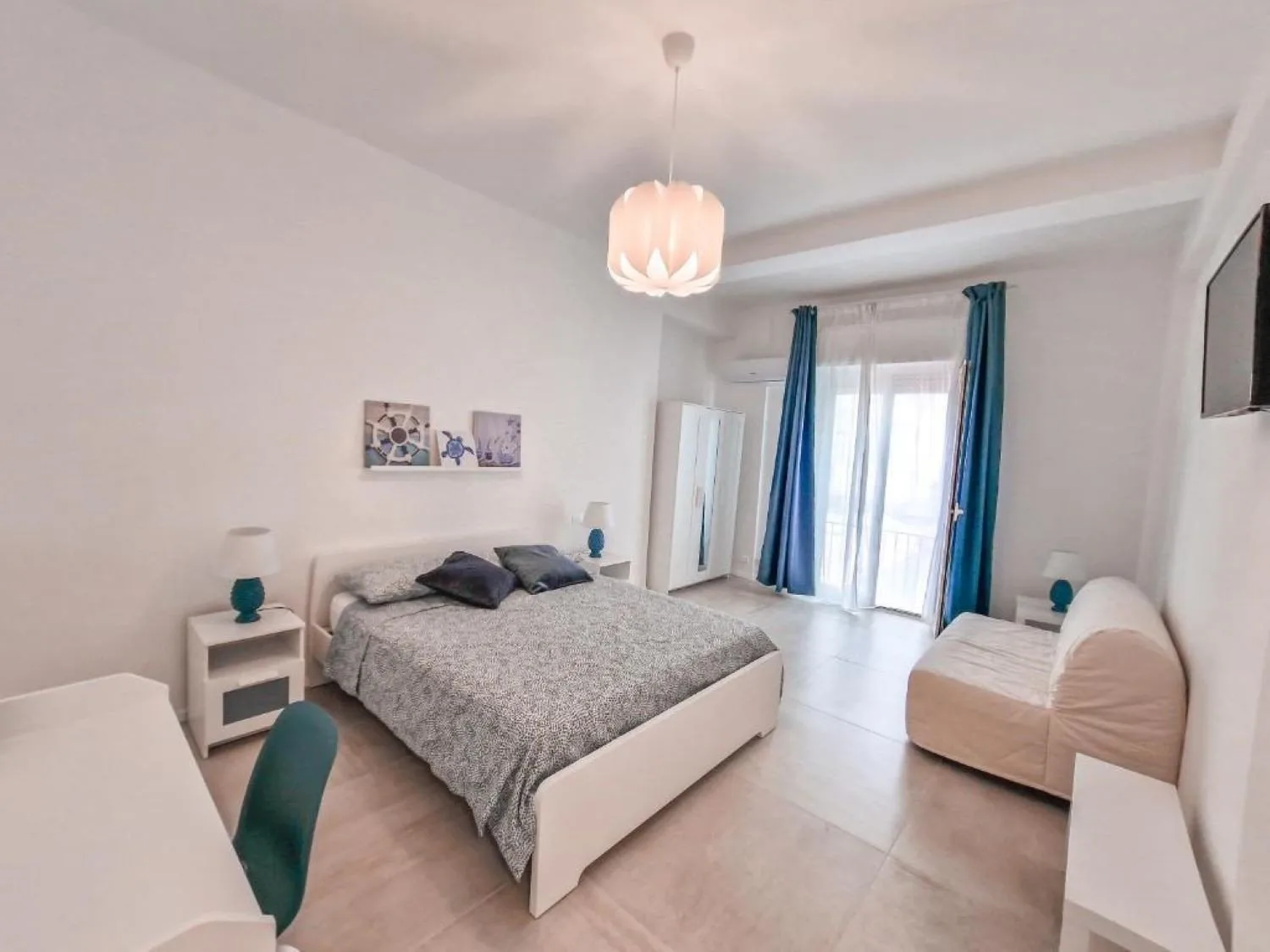 A bedroom with a bed, teal curtains, and a small upholstered seat.