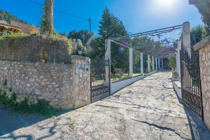 An open gated driveway leads beneath a vine-covered pergola.