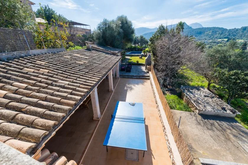 An outdoor swimming pool beside a tiled-roof building, with hills in the distance.
